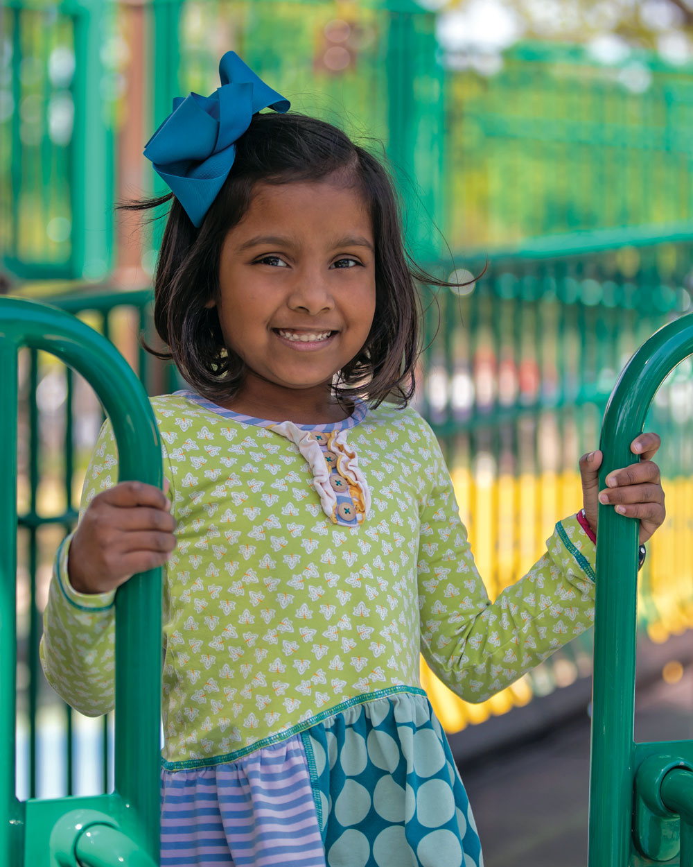 A young girl stands on a playground smiling at the camera.