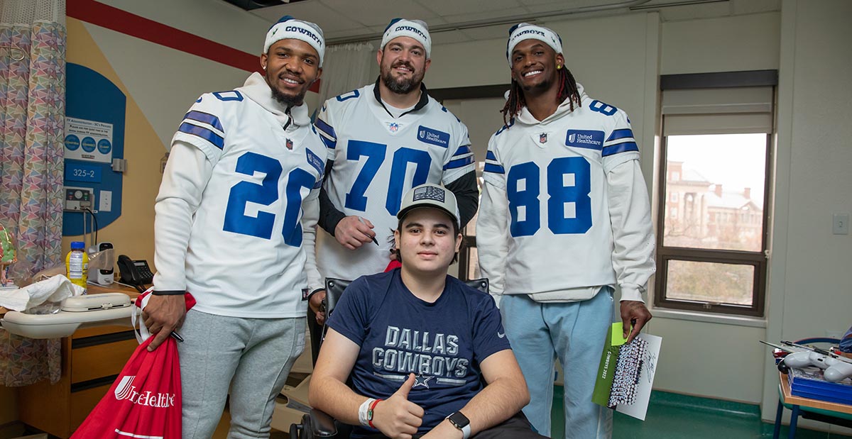 A boy wearing a dallas cowboys shirt gives a thumbs up