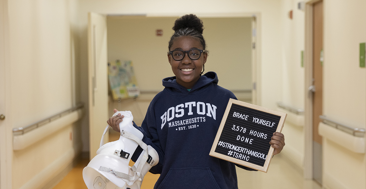 Neema in hallway with scoliosis brace and sign