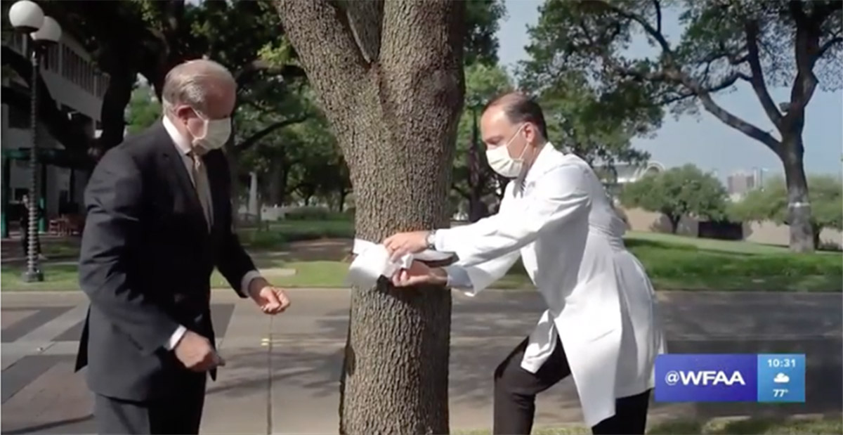 Two men wearing face masks are standing next to a tree and the time is 10:31